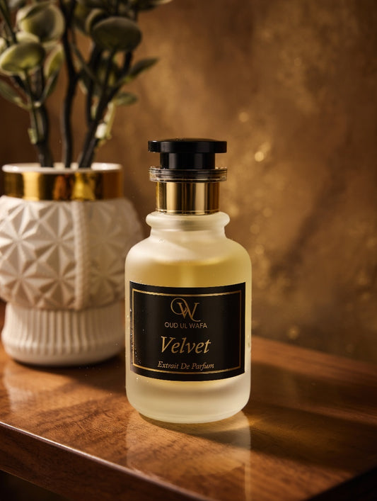 Perfume bottle labeled 'Velvet' by Oud & Wulf on a wooden surface with a blurred plant in the background.
